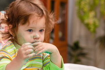 A one-year-old baby stained with paint looks thoughtfully in front of her. Children's creativity...