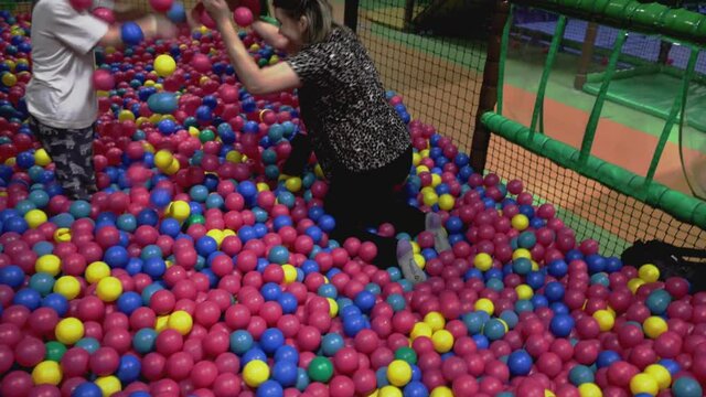Child and adult woman having fun in indoor ball pool in children activity center. 