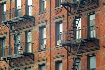 Gritty exterior of orange brick  tenement style apartment building with black fire escapes in central Manhattan, New York City - obrazy, fototapety, plakaty