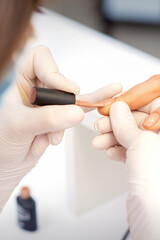 Hands of manicure master in white protective gloves apply polish to female fingernails