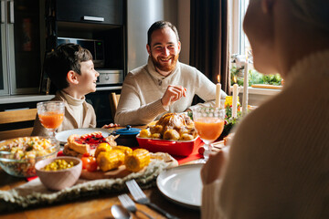 View from back of joyful young family enjoying at festive Christmas table during holiday family party. Cheerful mother, father and little son having dinner xmas party, eating and chatting at home.