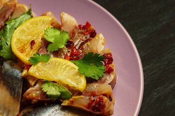 Herring fillet on a purple plate with spices, lemon, red pepper and herbs.