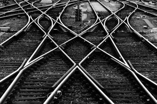 Railway tracks with switches and interchanges at a main line station in Frankfurt Main Germany with geometrical structures, thresholds, gravel and screws. Reflecting symmetrical rails black and white