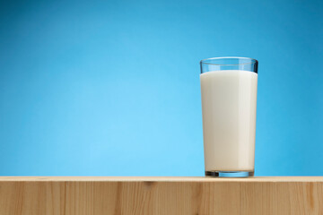 Glass of milk on wooden board with blue background, copy space