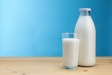 Bottle and glass of milk on wooden board and light blue background with copy space on the left.