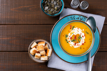 Butternut squash soup with cream, croutons and pumpkin seeds on one brown wooden table. Copy space. Top view.
