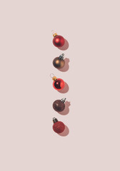 Minimal vertical flatlay composition with colorful shiny Christmas baubles lined up on sunny pink background.