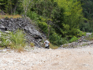 unidentified man with camera walking up hill on rock path in forest. nature travel. mountain trekking. 