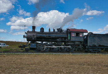 Obraz premium View of An Antique Restored Steam Passenger Train Blowing Smoke and Steam on a Sunny Day