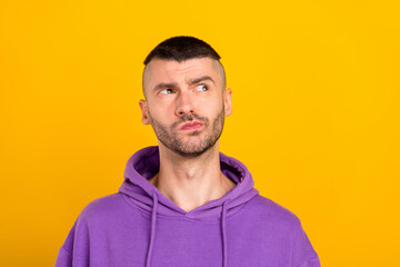 Photo of serious millennial brunet guy look empty space wear violet hoodie isolated on yellow color background