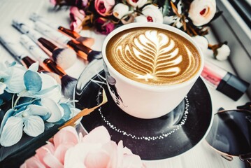 Cup of coffee, pink and blue flowers on a wooden white background with makeup brushes