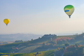Aerostatic balloons are flying over the hills of Langhe (Piedmont, Northern Italy), covered by vineyards during fall season; UNESCO Site since 2014.