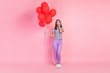 Photo of attractive impressed young woman dressed striped clothes holding many red balloons arm cheek isolated pink color background