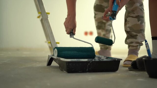 Unrecognizable workers hand mixes white paint with roller in plastic construction pallet, prepares to paint walls. DIY repair. Home workshop