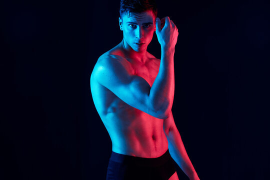 sexy guy with athletic physique posing on a black background and holds his hand near his face
