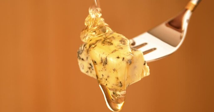 Liquid Organic Honey Dripping on a Fork with Dorbly Cheese on a Light Background. Healthy Food Concept. Golden Honey Pouring and Flowing on Cheese with Green Mold