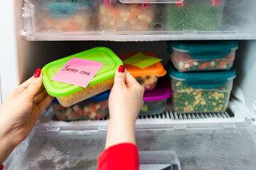 Woman placing container with frozen mixed vegetables in freezer.