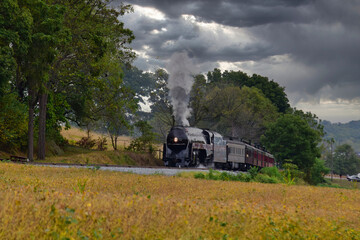 Fototapeta na wymiar An Antique Steam Engine Approaching With Passenger Coaches on an Overcast Fall Day