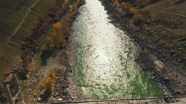 Aerial view of the calm mountain river Katun. Autumn landscape of the wild nature of the Altai Territory: Mountains, forests, fields, a country walking road, the rays of the sun. The camera flies