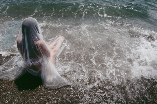 Rear view of a woman in a wet wedding dress sitting in sea