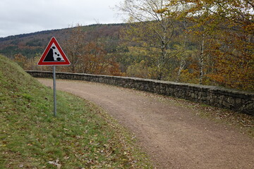 Hiking trail around Lake Primstalsperre water reservoir and falling rocks warning sign on a grey...