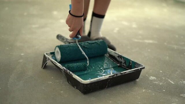 Womans hand wets a roller in a tray with blue paint. Creativity and home renovation concept. Finishing and decorating tools