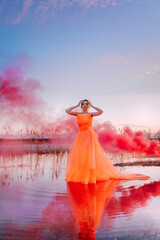 fabulous photo shoot of a girl in a long dress with pink smoke on the water