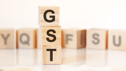 wooden cubes with letters GST arranged in a vertical pyramid, on the light background, reflection surface, concept