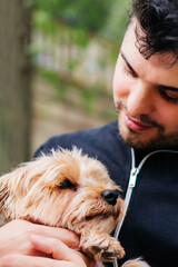 Vertical image of a young adult 20s hugging his Yorkshire terrier dog outdoors.