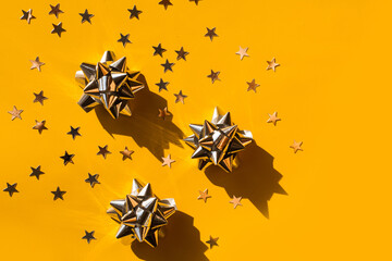 Gift silver bow with stars composition on monochrome yellow background. Winter, sale and seasonal concept. Merry Christmas, New Year banner. flat lay, top view. Space or place for text