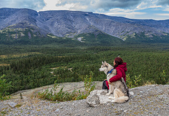 Fototapeta premium Young female sitting with siberian husky dog in mountains