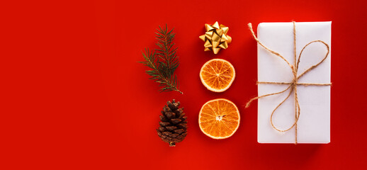 Christmas composition with eco crafted gift, dried orange, cone, xmas tree, gift and gold bow. Natural and minimal new year concept, top view, isolated, flat lay, copy space on red background, banner