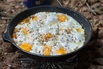 Shakshouka, a traditional dish of poached eggs in a sauce of tomatoes, harissa, olive oil,  onion,  garlic, spices and goat cheese, boiled in a pot outdoors 