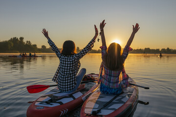 Beautiful rear view of two people on sup boards which floating on the river at sunset