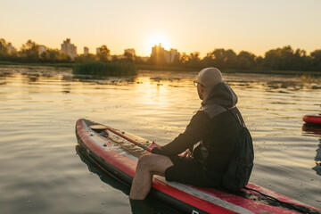 A man on a sup on the background of the river in the rays of the sunset