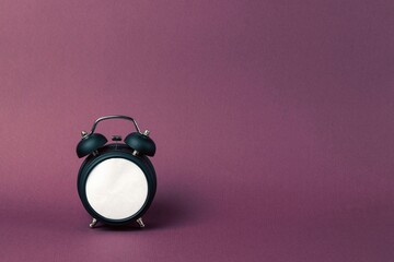 Black alarm clock in retro style on a purple background. Blank white dial.
