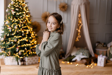 Beautiful cute little girl decorates the Christmas tree. A 10-year-old girl is smiling. New Year's atmosphere. Interior in natural colors. Portrait of a child for the new year. Sincere smile lifestyle