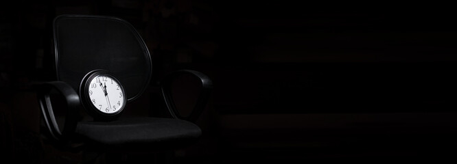 Deadline concept, time management. Clock on an office chair on a black background. Banner. Place...