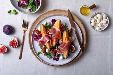 Fresh cantaloupe melon salad with prosciutto, figs, green leaves mix and mozzarella cheese. Top view, overhead, flat lay