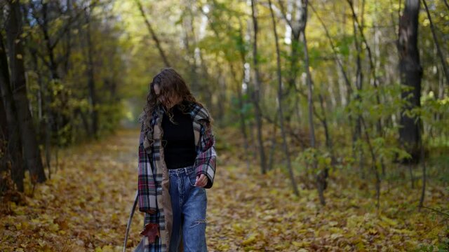 unhappy lonely woman is wearing jeans and coat is walking in woodland in fall day