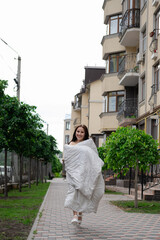 pretty brunette woman in white blanket on the street. crazy beautiful millennial carefree girl