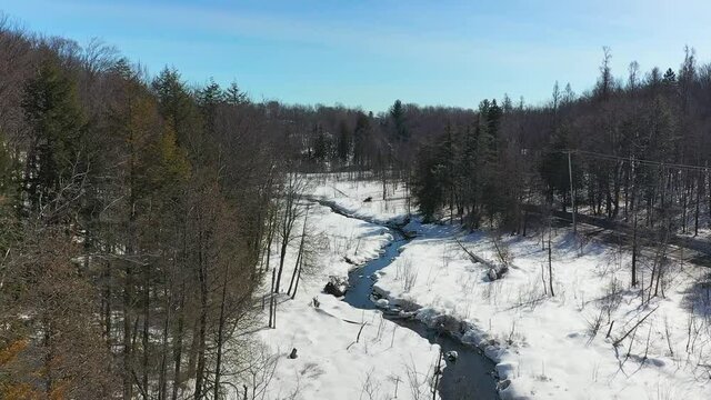 Aerial view following the small stream slowly melting in the sping and showing ducks playing in the fresh water in the Laurentians