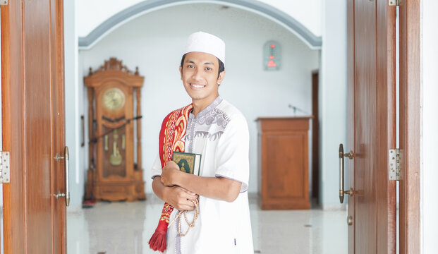 Portrait of a smiling man standing in a mosque holding prayer beads and the quran after prayers