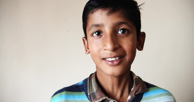 A smiling Indian boy standing against a white wall while smiling at the camera
