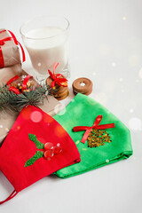 Handmade gift boxes, milk for Santa, cookies, protective face mask with holly and Xmas decoration on white background close up view. Winter holiday concept. Greeting card, frame