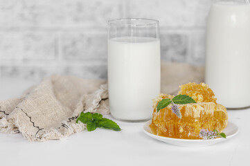 A still life of honey in honeycombs, a mint flower, a glass and a bottle of milk on a light background.