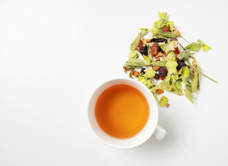 A cup of herbal tea with scattered dried herbs and pieces of fruit on a white background. Top view and copy space