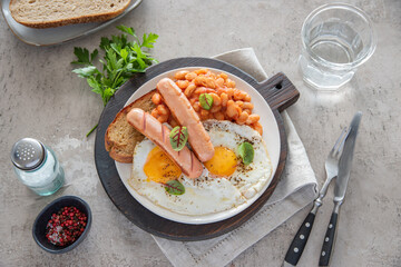 Traditional English breakfast with fried eggs, sausages, beans, fresh herb, red pepper and toast on a gray background. Concept morning and nutrition food. Top view