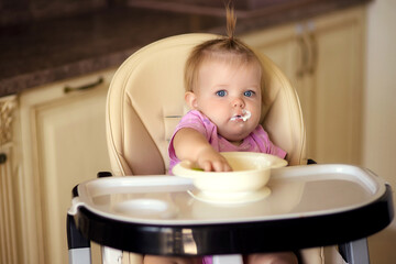 happy baby sitting at the table in the kitchen and eating with an appetite