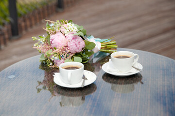 two cups of coffee. A bouquet of flowers and a cup of coffee on a glass table.